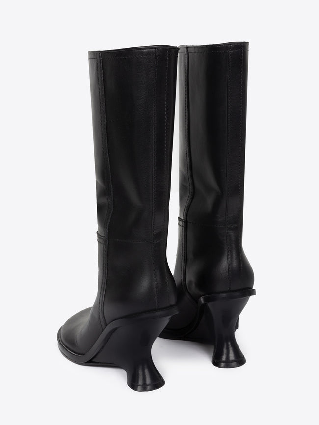 Backside of a pair of black leather wedge boots on a white background