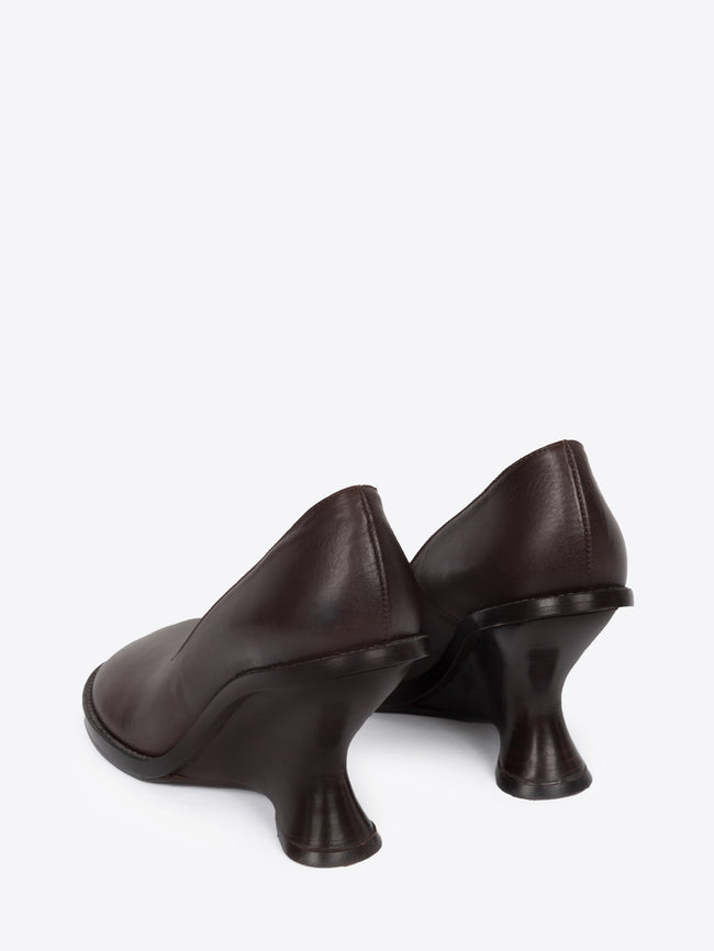 Backside of a pair of dark brown leather wedge pumps on a white background