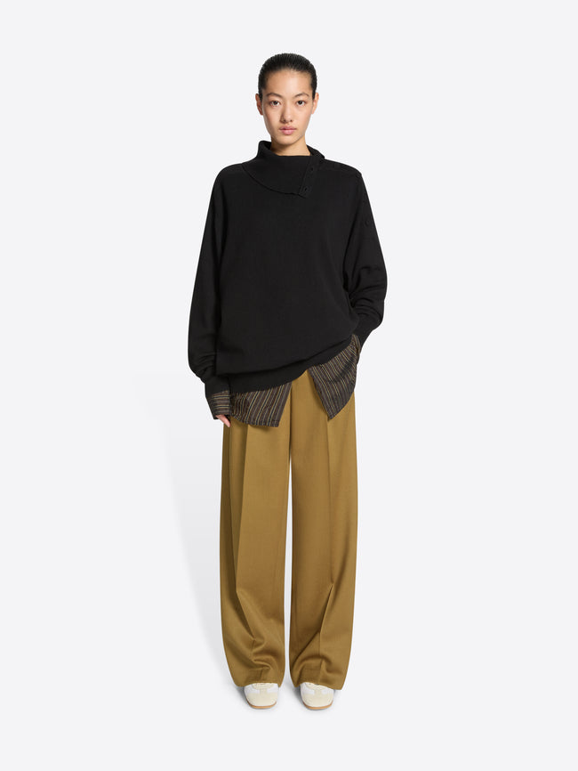 Person wearing a black sweater, mustard colored pants and a pair of white, with beige accents, suede sneakers on a white background