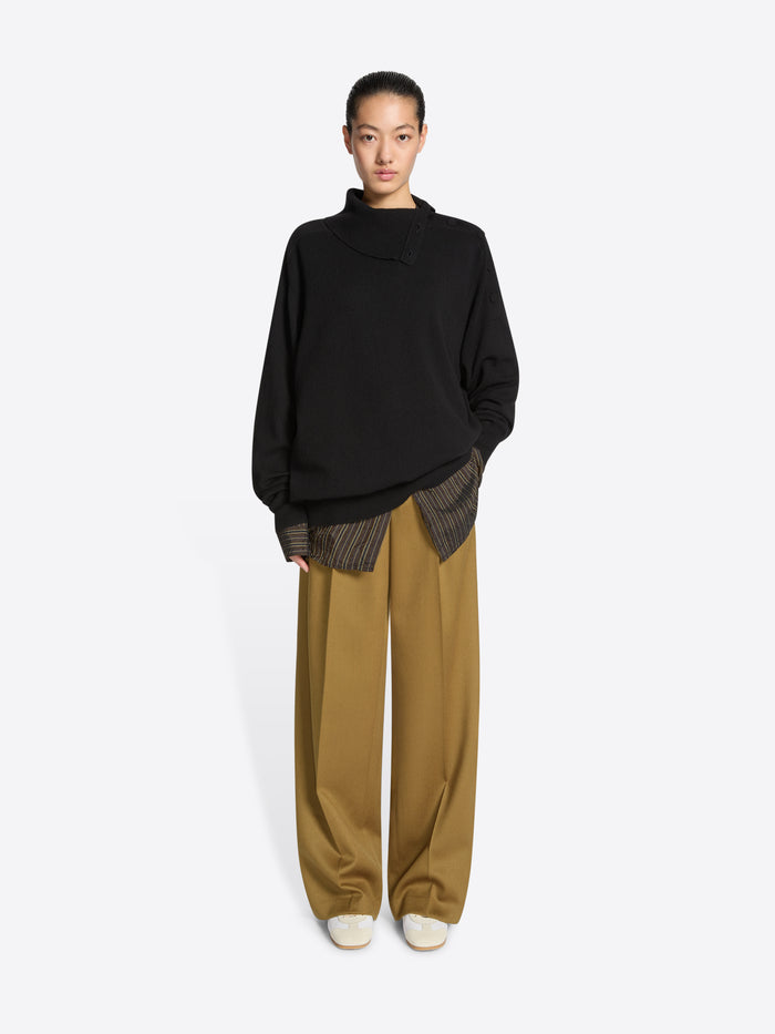 Person wearing a black sweater, mustard colored pants and a pair of white, with beige accents, suede sneakers on a white background