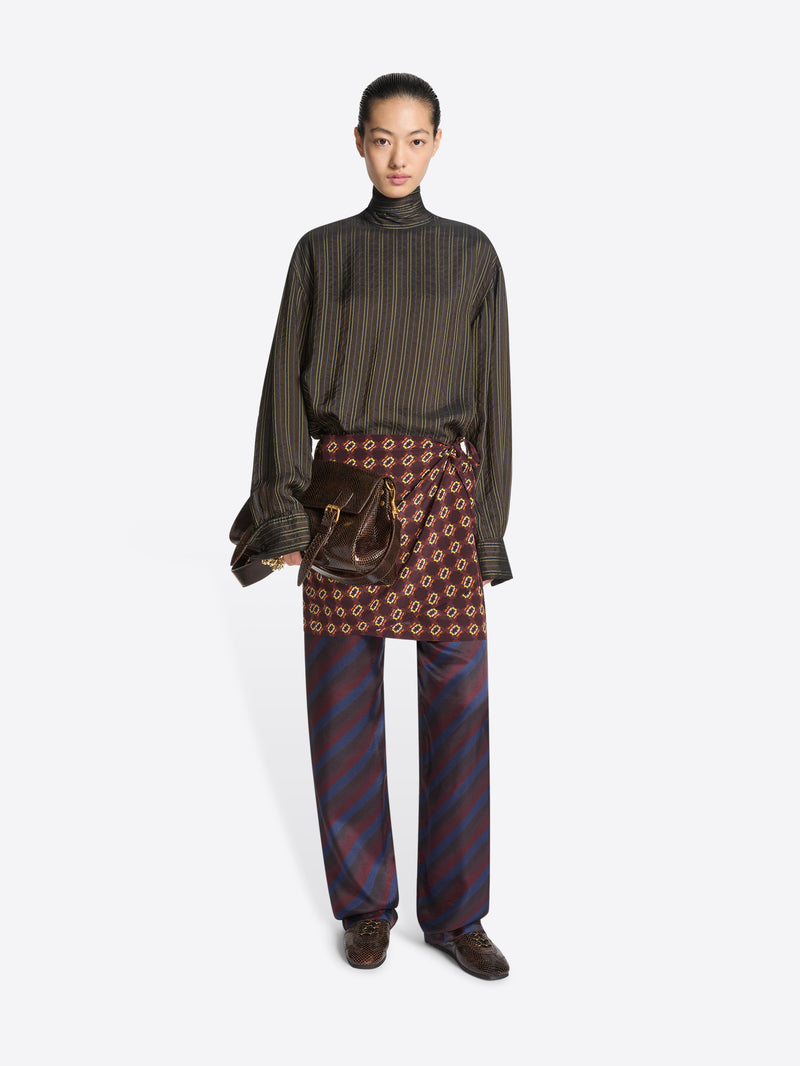 Person wearing a green striped top, multi color patterned skirtpants and a pair of brown suede sneaker with snake pattern on a white background