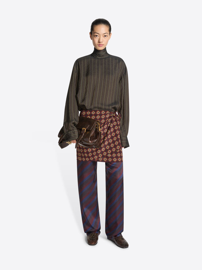 Person wearing a green striped top, multi color patterned skirtpants and a pair of brown suede sneaker with snake pattern on a white background