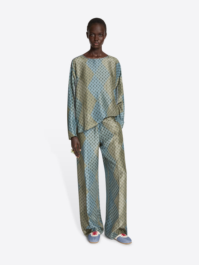 Person wearing a green and blue patterned ensemble and a pair of light blue nylon sneakers with red laces on a white background