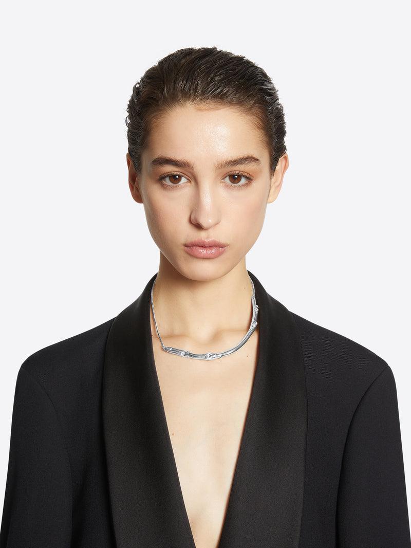 Person wearing a silver necklace with small round stones on a white background