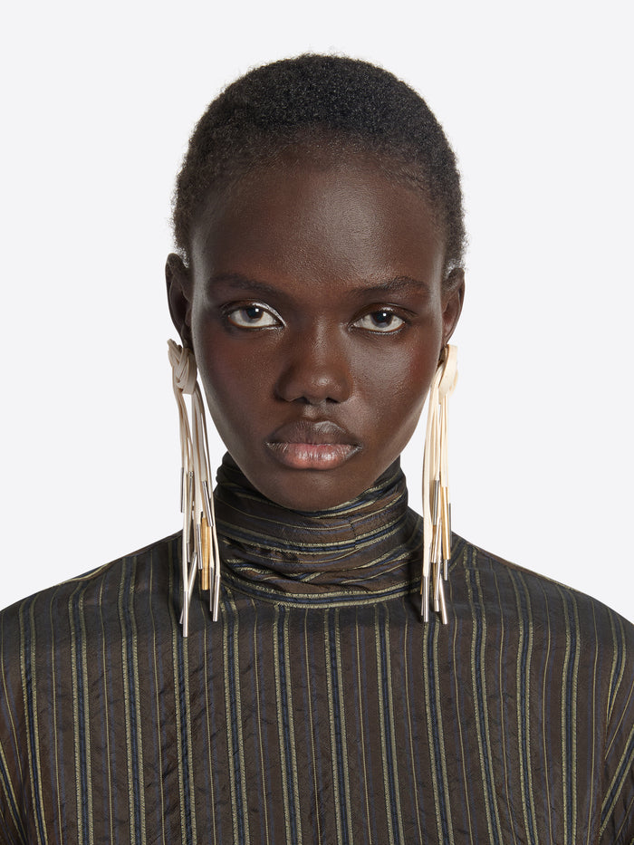 Person wearing a pair of earrings with multiple dangling strands on a white background