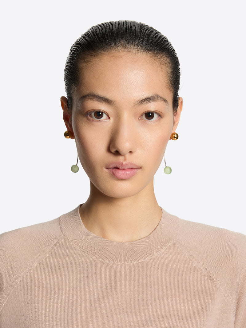 Person wearing a pair of earrings with gold and green beads on a white background