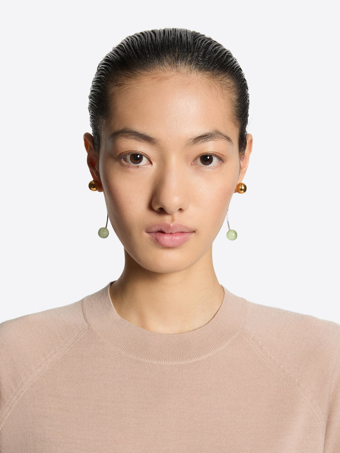 Person wearing a pair of earrings with gold and green beads on a white background