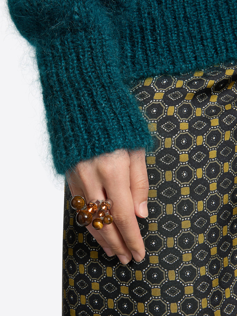 Close-up of a hand wearing a ring with brown beads, against a patterned fabric background.