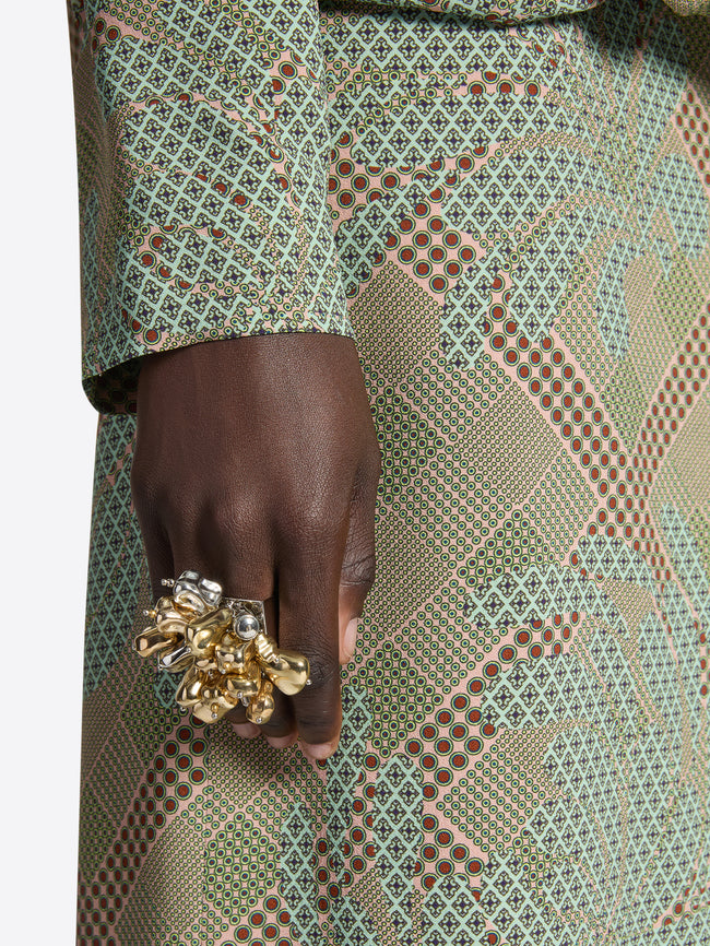 Hand wearing a gold ring with intricate design against a patterned fabric background
