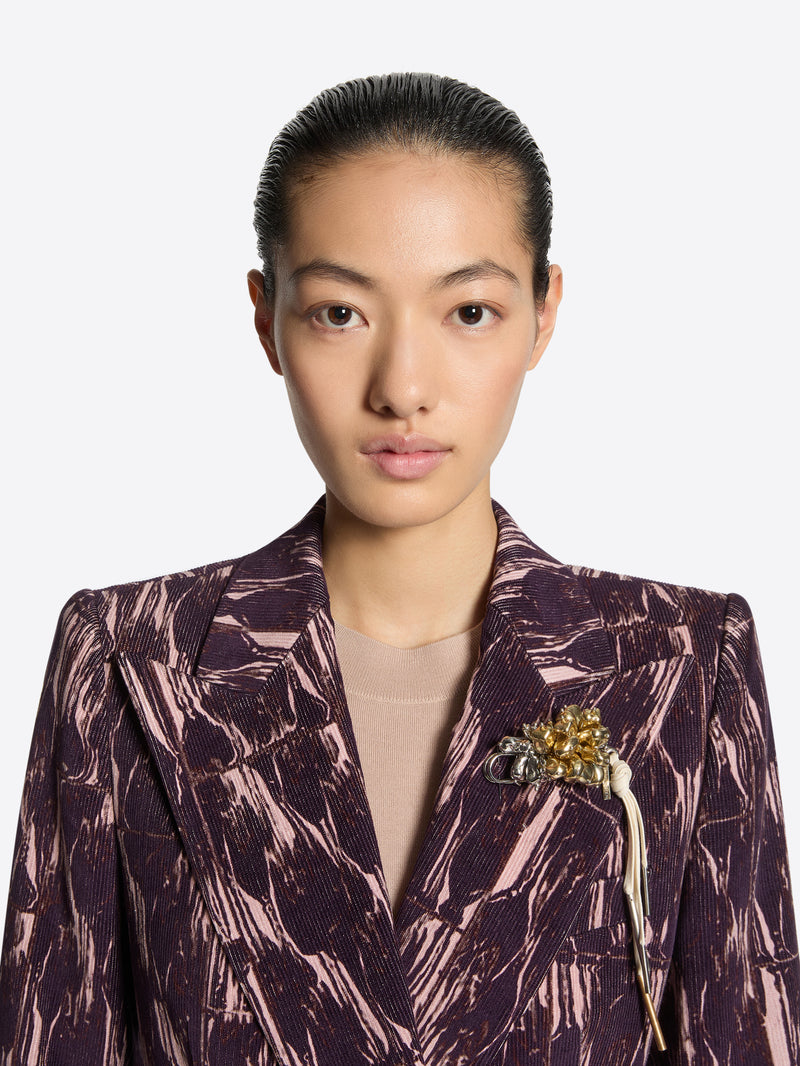 Person wearing a patterned jacket with a brooch on a white background