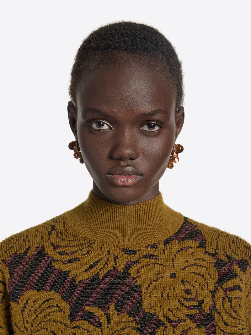 Person wearing a mustard yellow sweater with a floral pattern on a white background