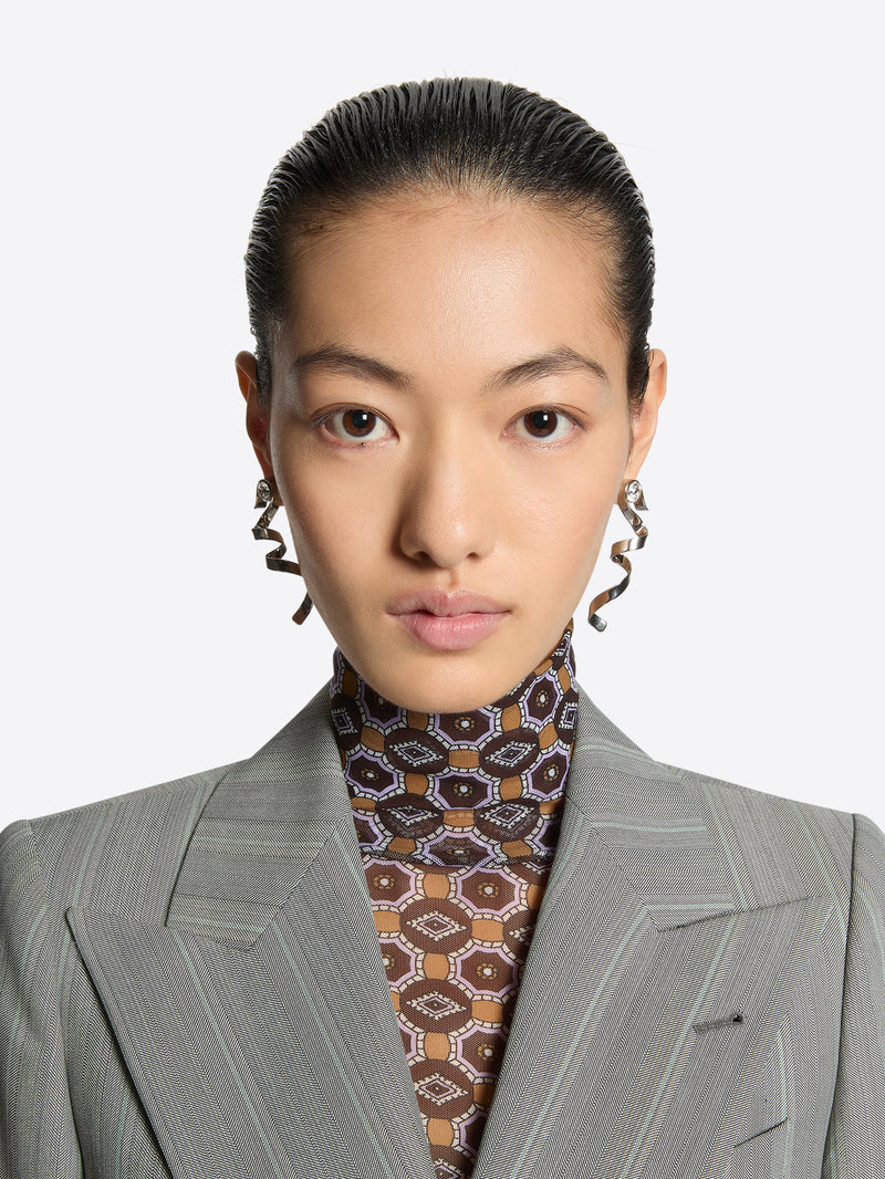 Person wearing a gray suit with a patterned shirt and earrings against a white background