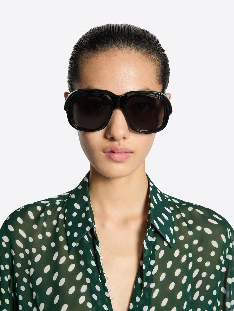 Woman wearing dark sunglasses with a green polka dot shirt on a white background