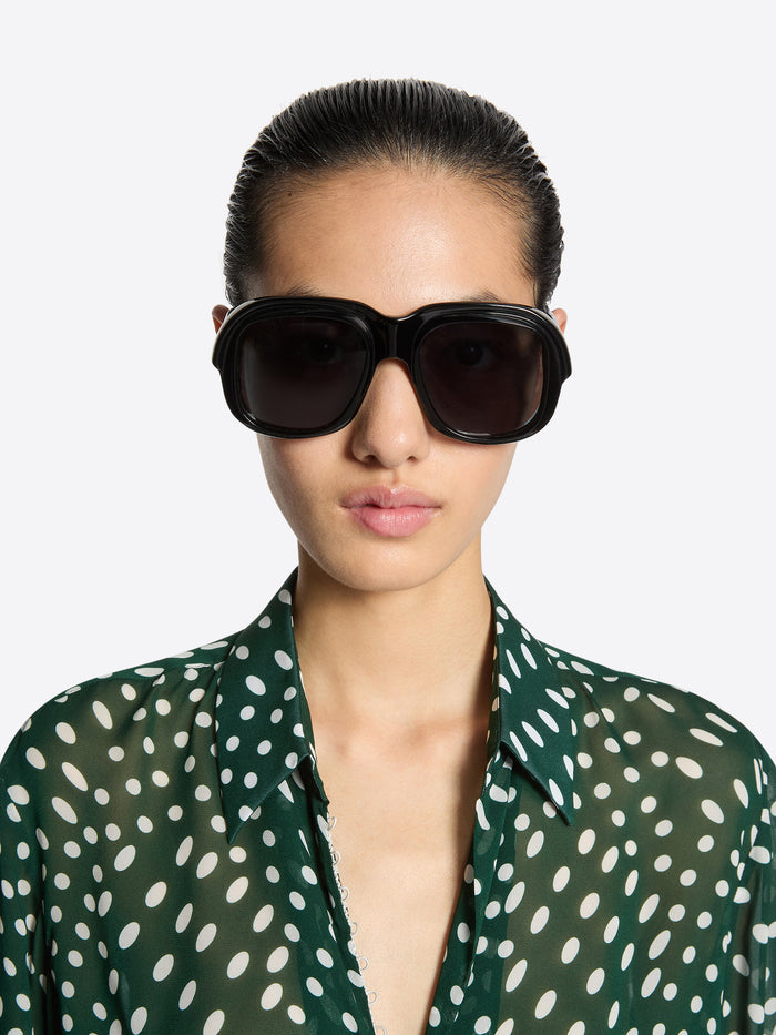 Woman wearing dark sunglasses with a green polka dot shirt on a white background