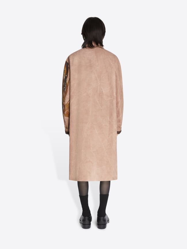 Person wearing a beige coat with floral embroidery on a white background