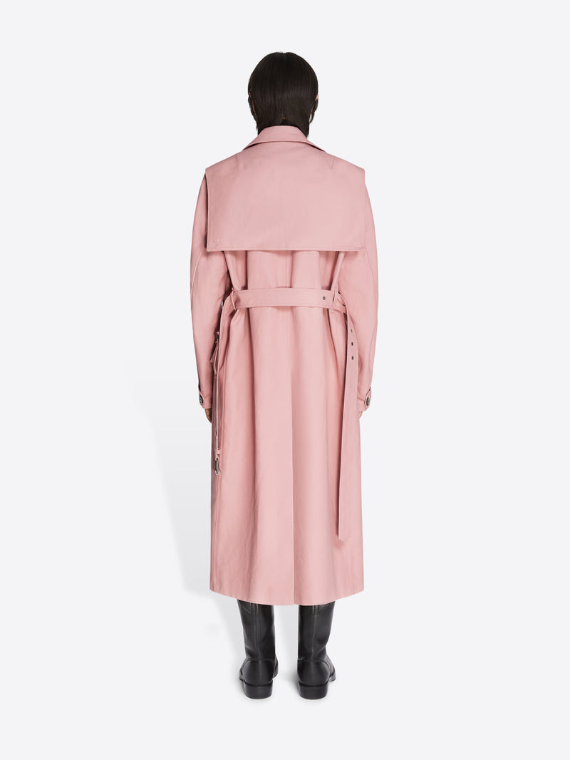 Backside of a model wearing black leather boots and a rose colored cotton trench coat on a white background