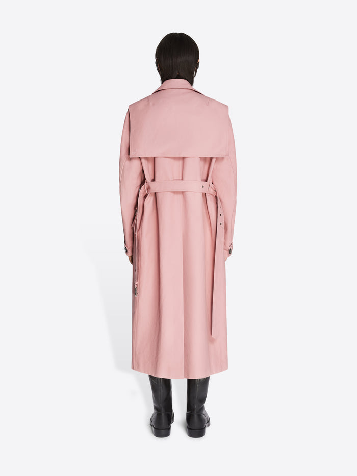 Backside of a model wearing black leather boots and a rose colored cotton trench coat on a white background