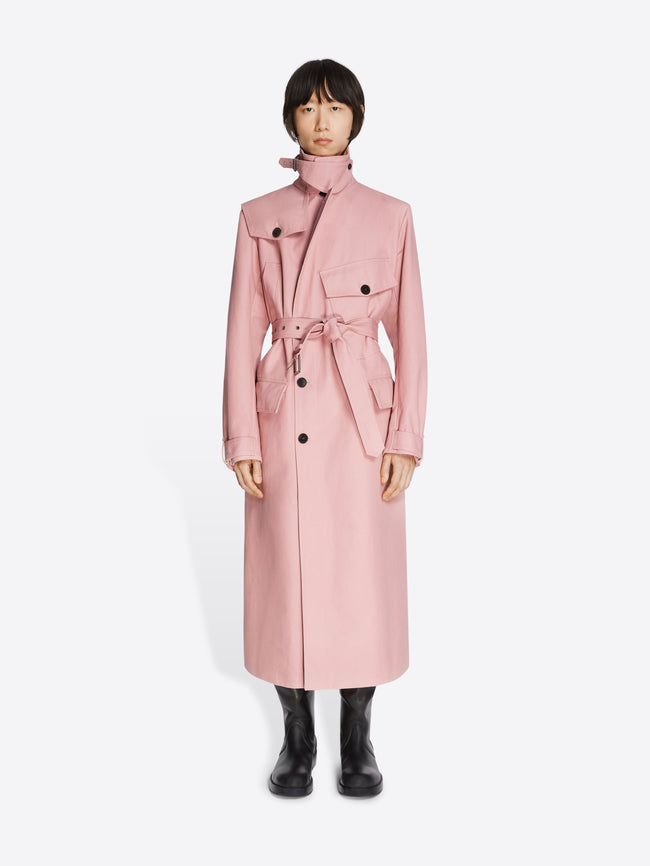 Model wearing black leather boots and a rose colored cotton trench coat on a white background