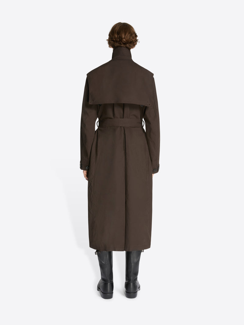 Backside of a model wearing a brown, overdyed trench coat and black leather boots on a white background