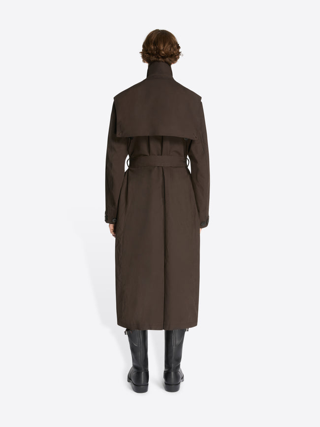 Backside of a model wearing a brown, overdyed trench coat and black leather boots on a white background