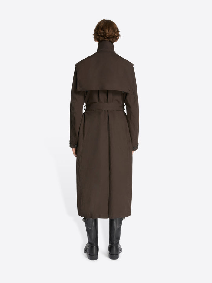Backside of a model wearing a brown, overdyed trench coat and black leather boots on a white background