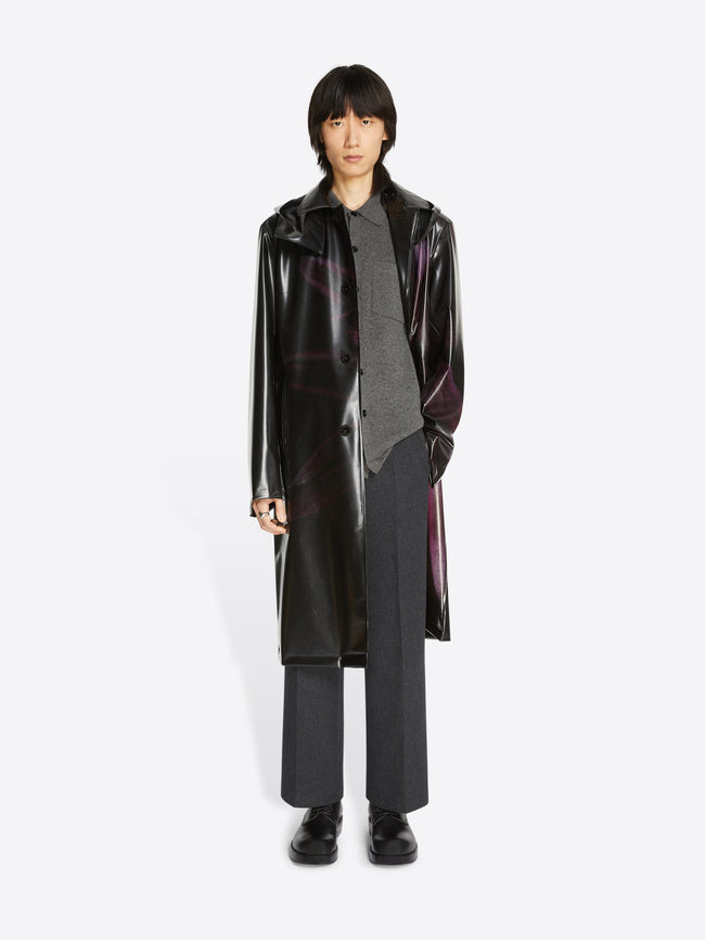 Person wearing a long black coat with a reflective quality on a white background