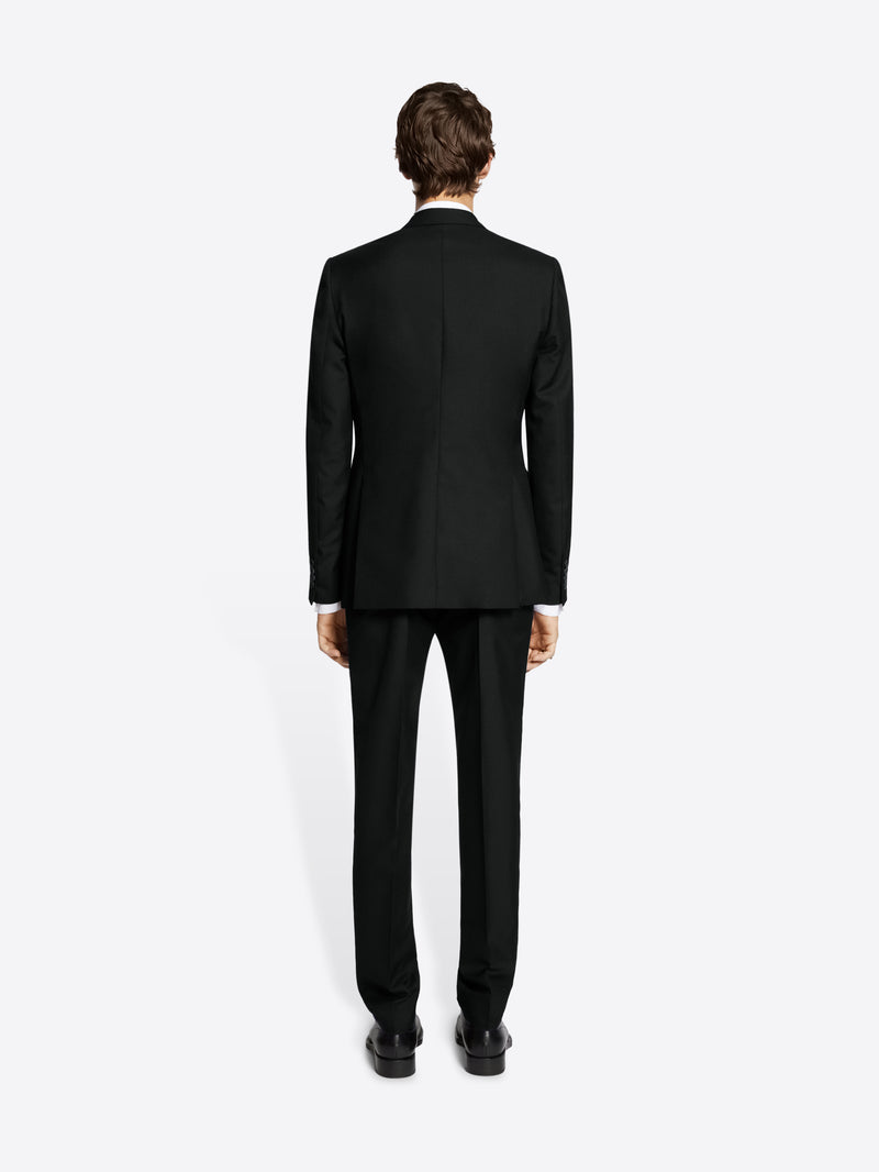 Person wearing a black suit and black derby shoes on white background