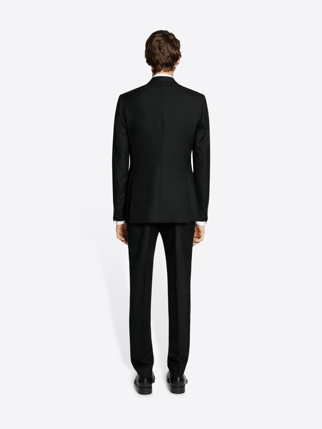 Person wearing a black suit and black derby shoes on white background