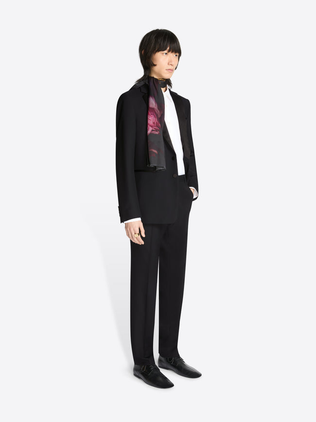 Person wearing a black, woolen, slim fit tuxedo, a white shirt and dark shoes on a white background