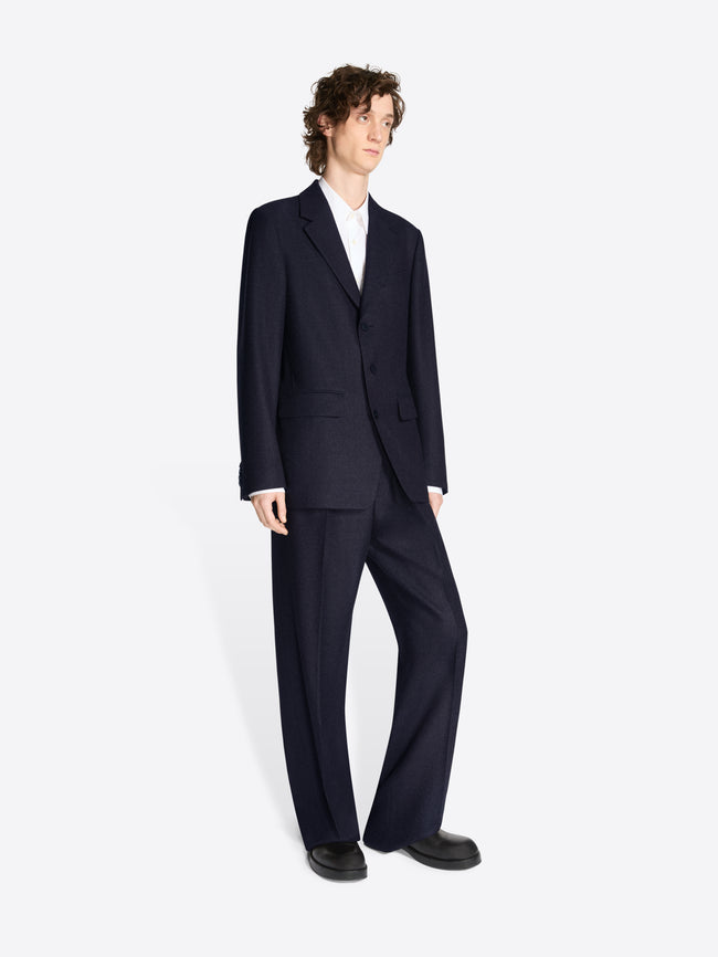 Model wearing a navy colored, loose fit suit on a white background