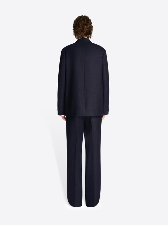 Backside of a model wearing a navy colored, loose fit suit on a white background