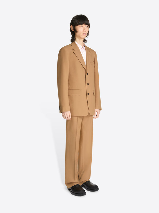 Model wearing a tan colored loose fit suit on a white background