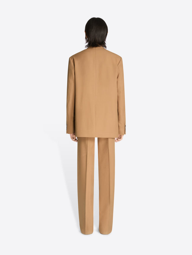 Backside of a model wearing a tan colored loose fit suit on a white background