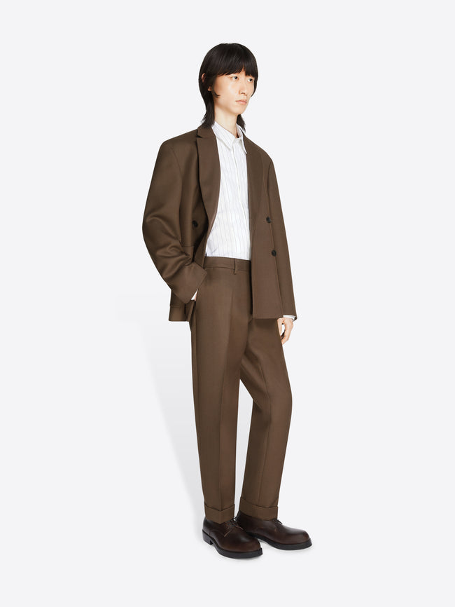 Model wearing a white shirt, mud colored, boxy wool blazer and matching pants on a white background