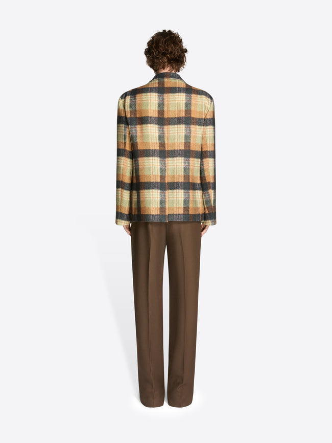 Backside of a model wearing brown pants, black leather boots and an ocra check patterned boxy wool blazer on a white background