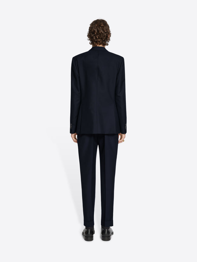 Person wearing a black blazer, black pants and black derby shoes on white background