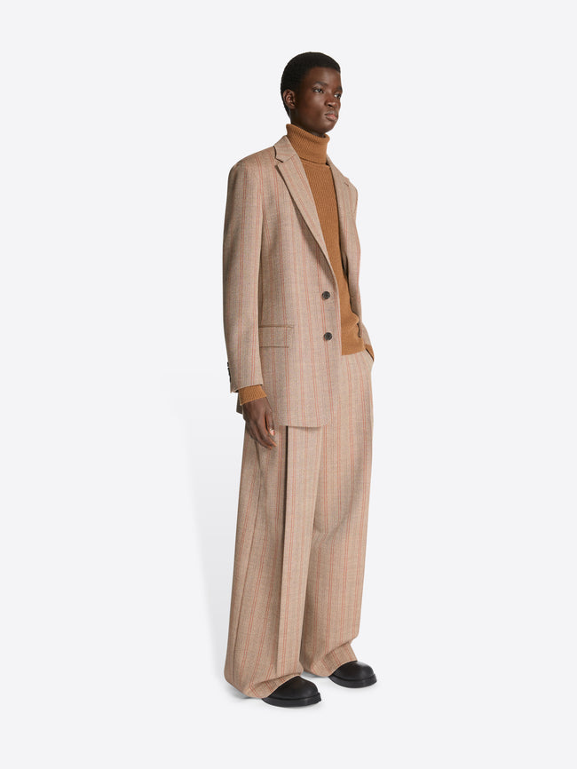 Person wearing a camel colored turtleneck, rust colored, striped, loose fit blazer and matching pants on a white background