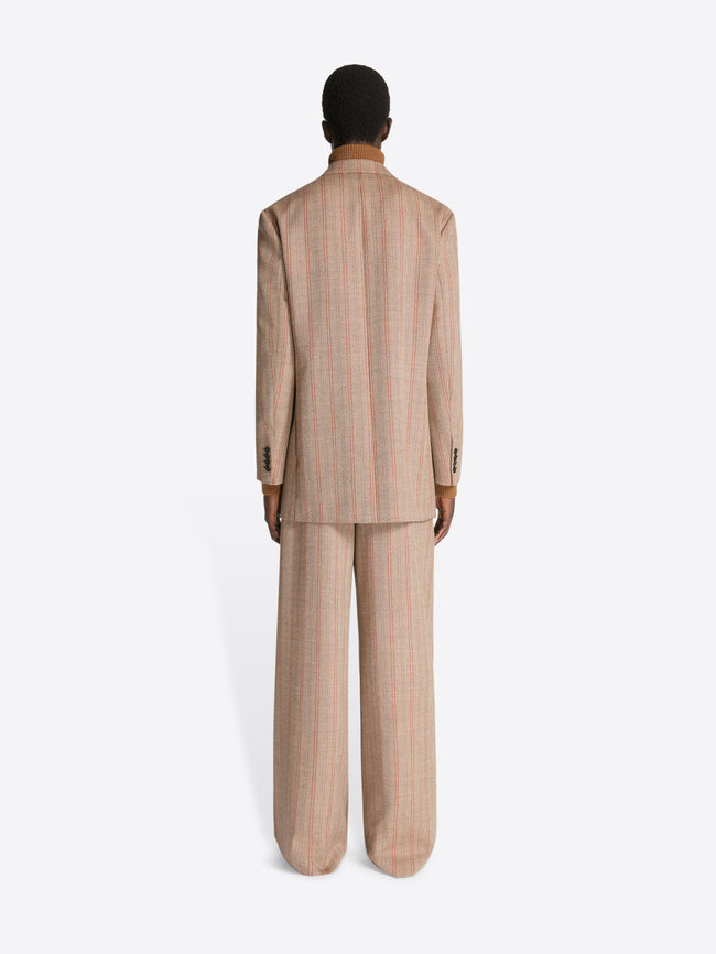 Backside of a person wearing a camel colored turtleneck, rust colored, striped, loose fit blazer and matching pants on a white background