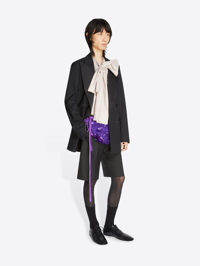 Model wearing a white top, black wool tuxedo jacket and matching shorts on a white background