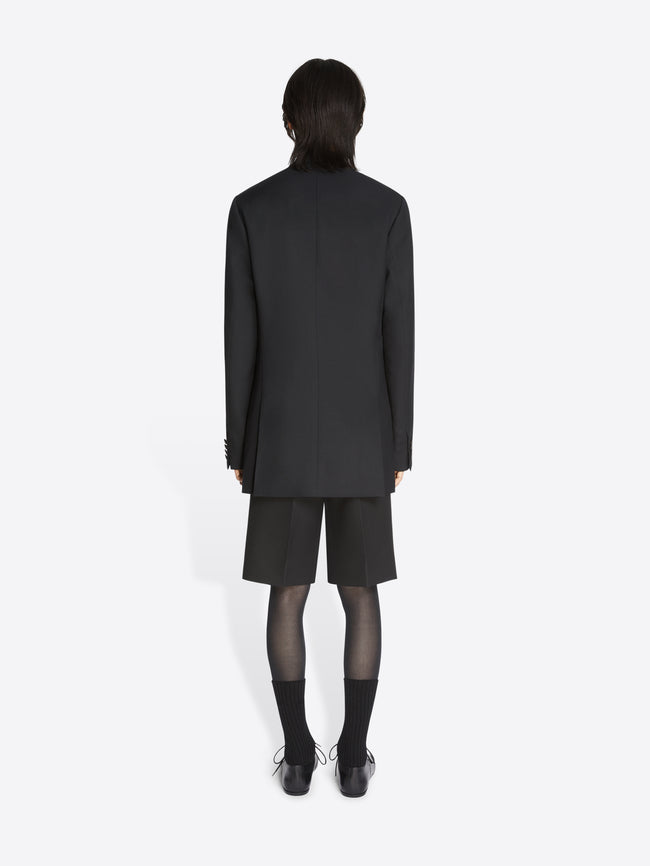 Backside of a model wearing a black, wool tuxedo jacket and matching shorts on a white background