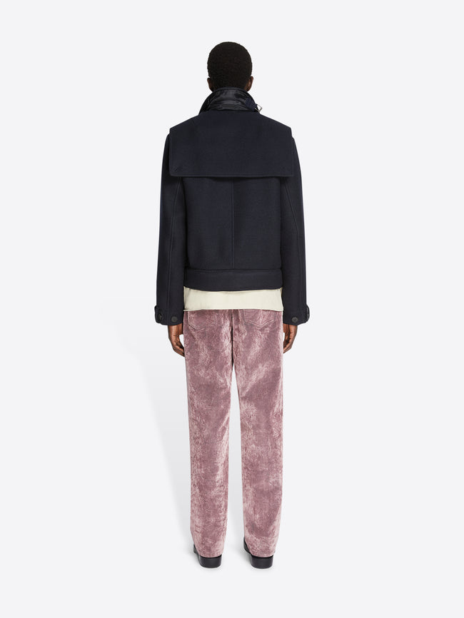 Backside of a person wearing a white shirt, midnight colored, short wool trench coat and pink pants on a white background