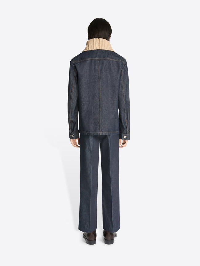 Backside of a person wearing a dark denim shirt jacket and matching pants on a white background