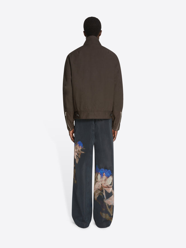 Backside of a model wearing a brown overdyed shell jacket and black floral pants on a white background