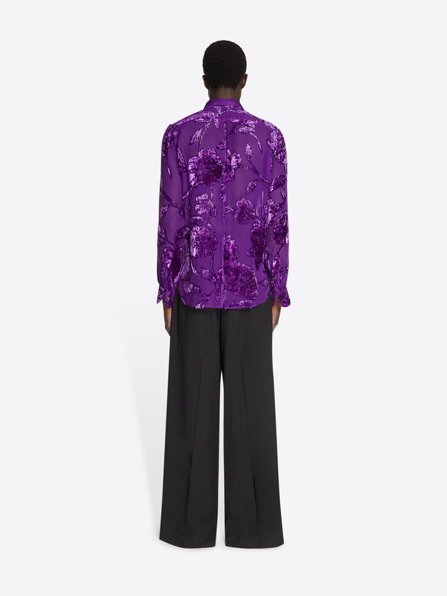 Backside of a model wearing a purple fitted sheer shirt and black pants on a white background