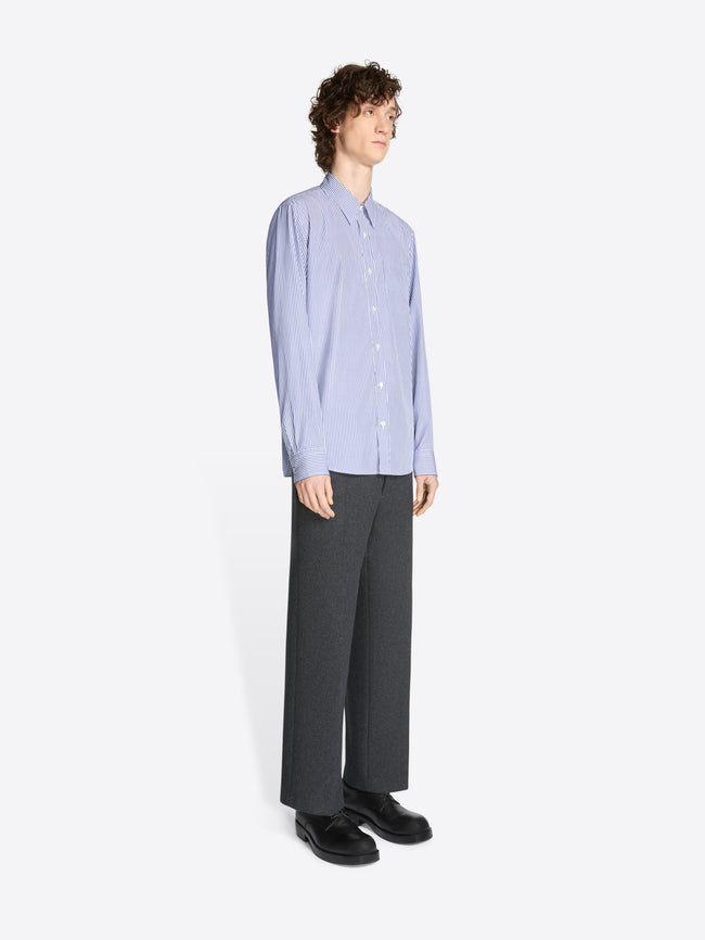 Model wearing a white and navy striped fitted cotton shirt and grey pants on a white background