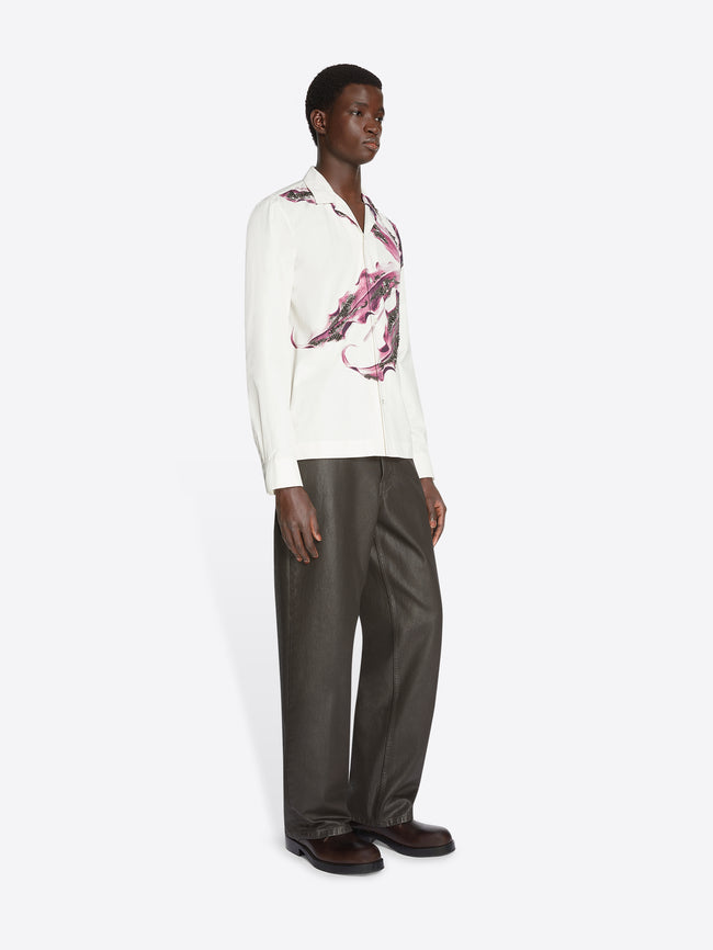 Model wearing a white, floral embroidered cotton shirt and grey pants on a white background