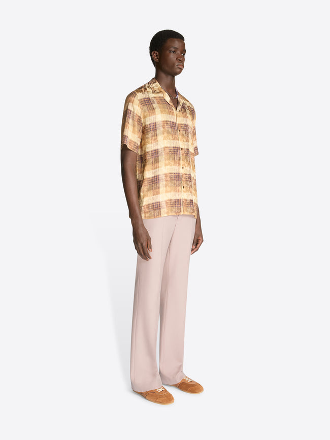 Model wearing a tan check print boxy shirt and light pink pants on a white background