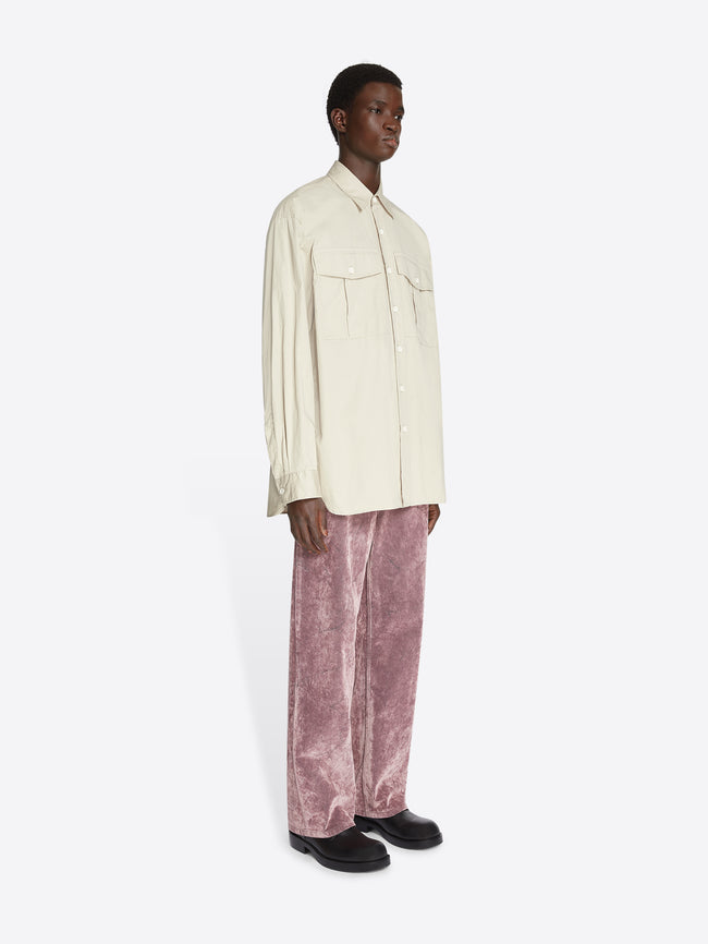 Model wearing beige colored oversized cotton shirt with chest pockets and dusty pink pants on a white background