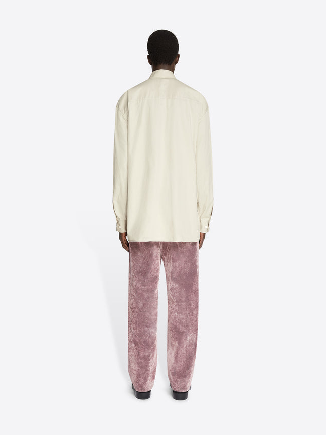 Backside of a model wearing beige colored oversized cotton shirt with chest pockets and dusty pink pants on a white background