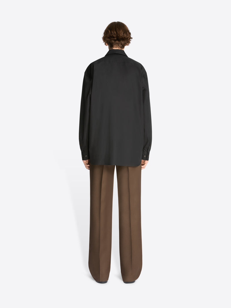 Backside of a model wearing a black cotton shirt and brown pants on a white background